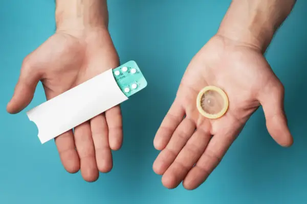 Deux mains ouvertes présentent une plaquette de pilules contraceptives et un préservatif, symbolisant les options de contraception hormonale masculine.